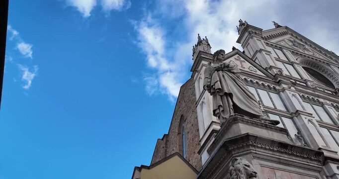 Low-angle shot of Santa Croce in Florence featuring the marble statue of Dante Alighieri by Enrico Pazzi. Gothic facade, laurels, and book highlight the poet&rsquo;s legacy.
