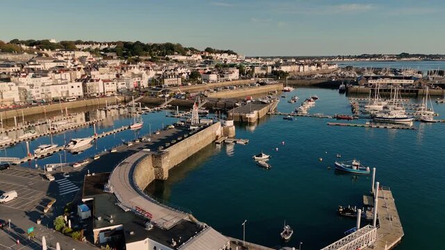 St Peter Port Harbour Guernsey drone flight over Albert Marina Victoria Marina Crown Pier and careening hard in late afternoon sun with backdrop of the town and Belle Greve Bay in the distance