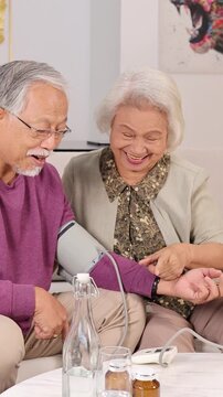 Elderly Asian Couple Checking Blood Pressure Together in Vertical Framing