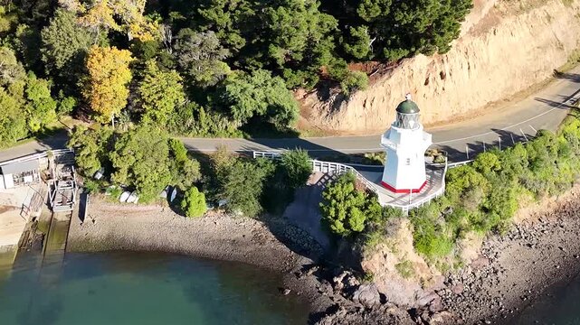 Aerial View of Akaroa Lighthouse on Rocky Coastline with Lush Greenery