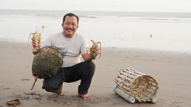 balinese fisherman with two lobsters in tabanan, bali, indonesia, caught at sea using traditional bamboo trap or pot, indonesian people, portrait smiling, looking at camera