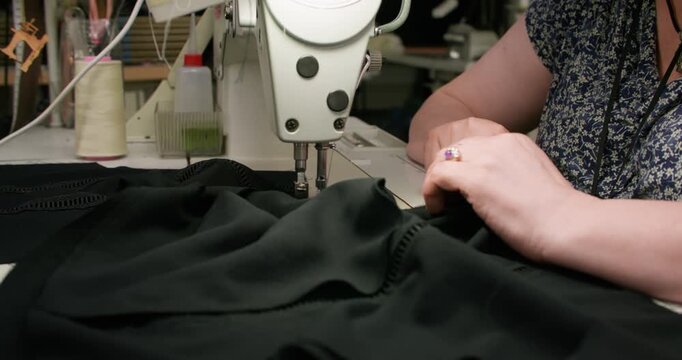 Tailor workshop. Textile craft. Female hand sewing black clothes on stitching machine. Making thread seam on fabric occupation.