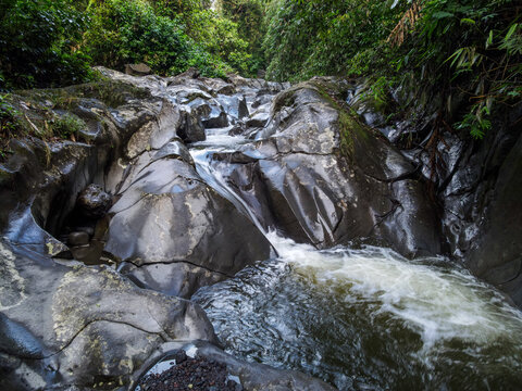 Aerial view of Waterfall cascading over smooth stones in a tropical jungle, Clear mountain stream running through a rocky riverbed, Nature landscape with a babbling brook and vibrant green foliage