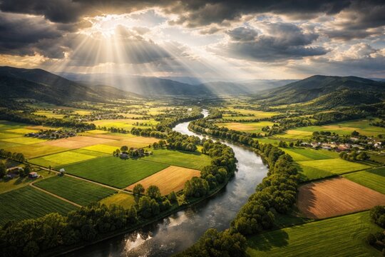 Aerial drone panorama of farmland with hills and river under godrays and clouds