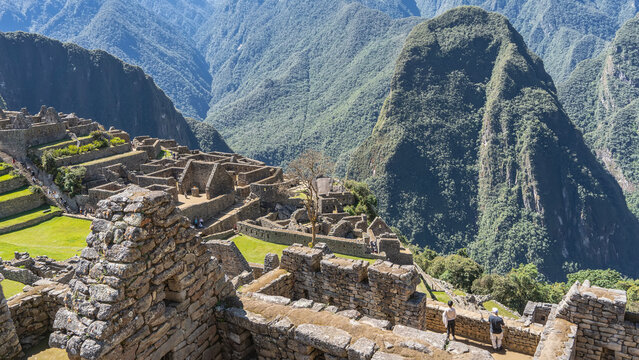 Ruins of ancient Lost City of the Incas Machu Picchu. Dilapidated stone buildings, terraces, stairs on the mountainside. People are walking. Majestic Huayna Picchu, the Andes mountain range. Peru.
 