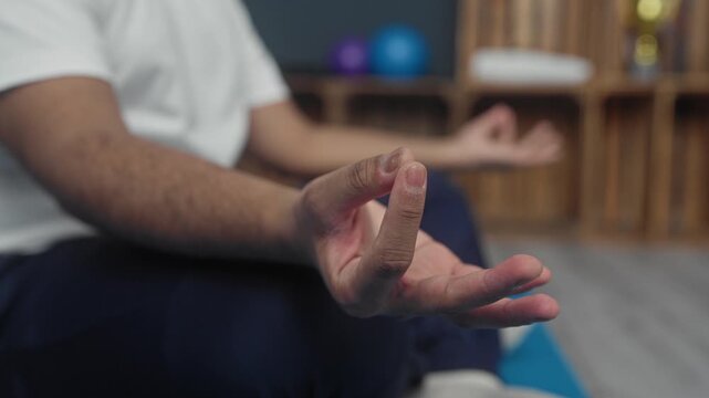 Man seated on yoga mat with hand and fingers forming meditation mudra while seated in studio yoga class; calm mindfulness.