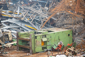 Industrial scrap yard with piles of metal debris, including a green machine and twisted steel, showcasing a chaotic environment of discarded machinery and materials