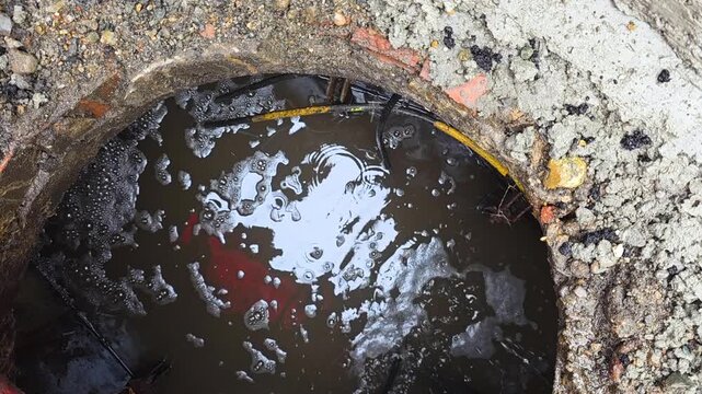Reflective Oily Water In Drain Cavity Shimmering Surface Reveals Contamination And Trapped Leaf Litter, Gritty Concrete Rim With Sediment, Urban Runoff Hazard, Environmental Concern