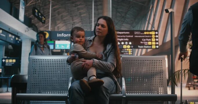 Mother and Father With Two Toddlers Arrive at Airport Waiting Hall With Suitcases. Father Actively Manages Travel Logistics Via Mobile Device, Mother Comforts and Manages Kids. Lifestyle of Traveling.