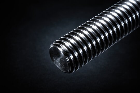Close-up of cylindrical metallic threaded rod with deep grooves on dark background with copy space