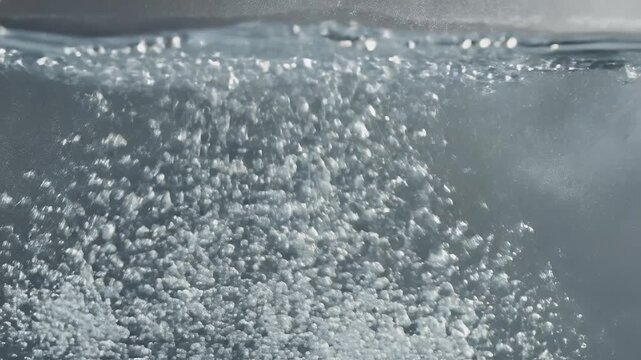 Bubbles rise and burst at the surface of dark, agitated water