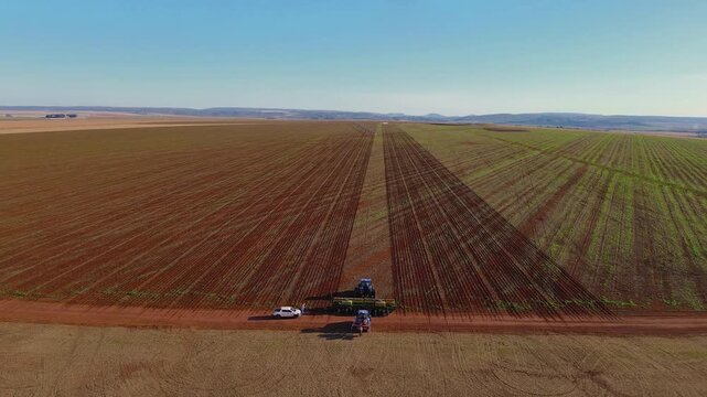 Aerial view of multiple tractors cultivating and planting long, neat crop rows across expansive Formosa, Goi&aacute;s fields, showcasing modern agribusiness machinery and fertile soil, drone pull away