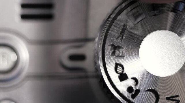 Macro close up of silver mode dial rotating on grey camera body with scene icons