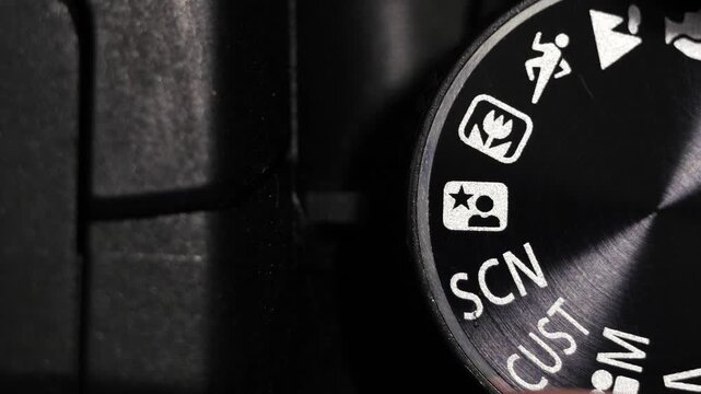 Top down macro of black mode dial rotating on black camera body with white icons