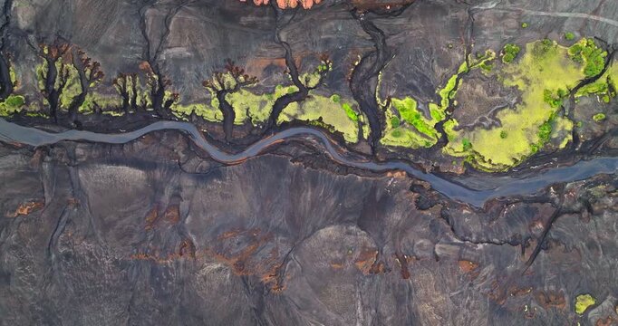 Vanuatu Tanna Island aerial view of a dark winding river cutting through volcanic ash, creating abstract contrasts with vivid green vegetation patches in a remote tropical landscape. Top down flight