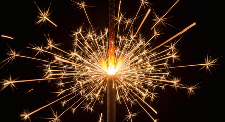 Fototapeta premium A close-up shot of a lit sparkler creating a burst of golden sparks against a black background.