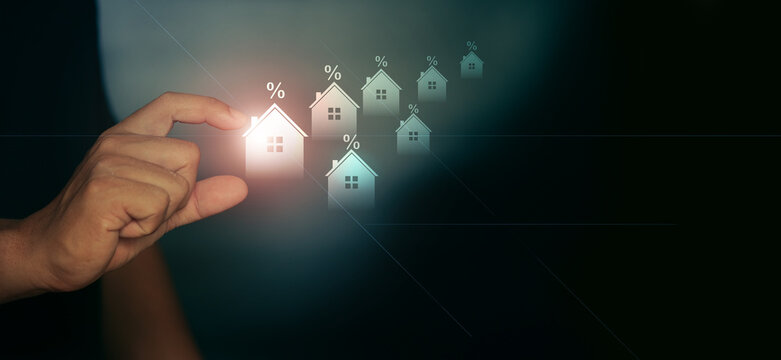Concept image of real estate investment with hand selecting house icon and interest rate symbols. Represents mortgage finance, housing market trends and property investment decisions.