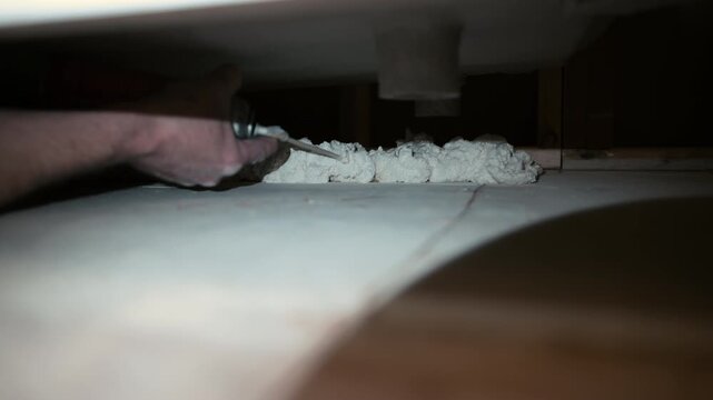 worker applying expanding foam insulation into a narrow gap under a structure. Construction or renovation process detail, sealing cracks for thermal insulation, air leakage.