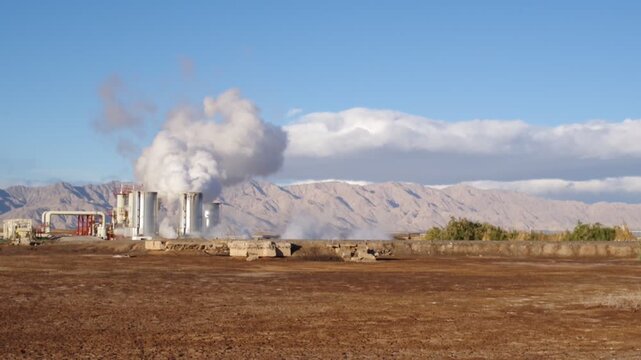 Campo geotermico en Mexicali Baja California Mexico. Zona de pozos para extraccion de vapor para generar energia electrica en el valle con cielo azul despejado y nubes sobre las monta&ntilde;as en el fondo