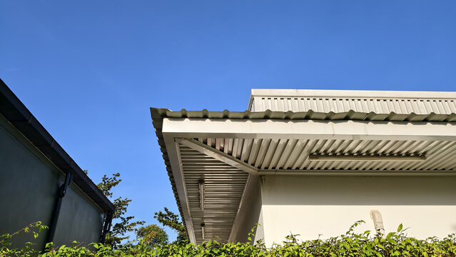 Modern building roof featuring white corrugated metal sheets and gutter system against clear blue sky. This architectural shot highlights clean lines industrial materials