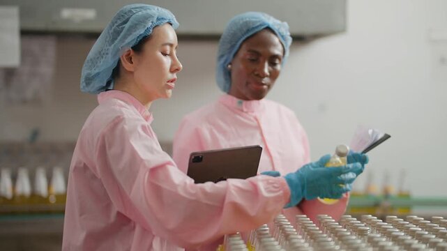 Teamwork on the Production Line: Two female workers in protective attire collaboratively examine product samples.