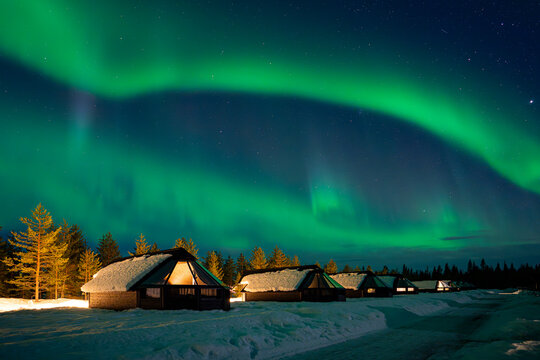 Snow-covered village, Lapland, Northern Finland, rural houses with glass roof, snow covered. Aurora borealis (also known like northern or polar lights) beyond the Arctic Circle. Levi, Finland