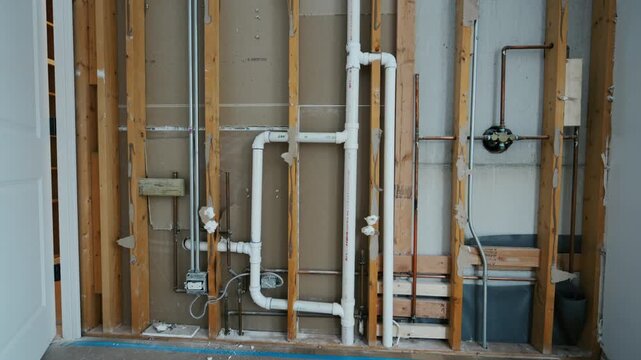 Wall framing with plumbing pipes during house renovation. Construction phase showing open studs, water supply and drainage system installation inside residential interior before drywall finishing.