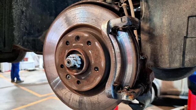 Close up of car disc brake system showing worn rotor, caliper, and pads in workshop setting, highlighting mechanical details, friction components, and automotive maintenance context