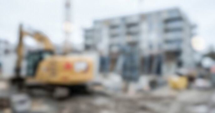 A construction site featuring heavy machinery, building materials, and an apartment complex in the background under a cloudy sky, showcasing ongoing development.