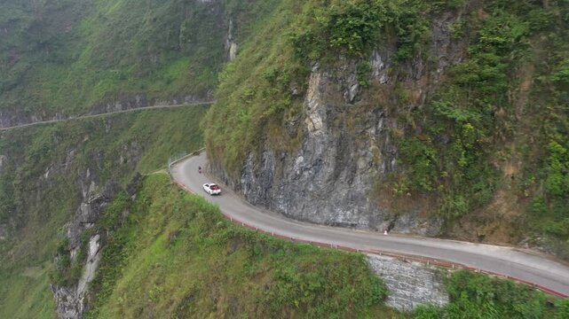 Aerial view of a pickup truck driving on a Ha Giang mountain pass through majestic rocky mountains