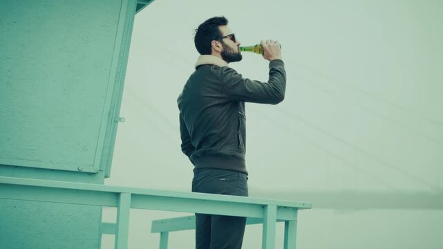 Traveler Drinking Beer From Bottle. Tourist Refreshing With Cold Lager On Misty Beach