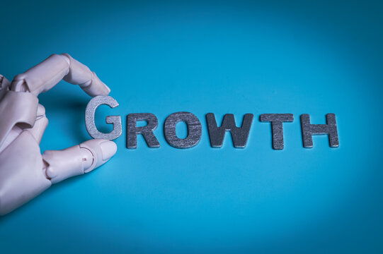 Robotic Hand Arranging Silver Letters to Spell Growth on Blue Background