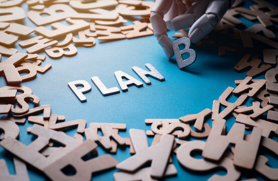 Robot hand arranging wooden letters to form Plan B on blue background
