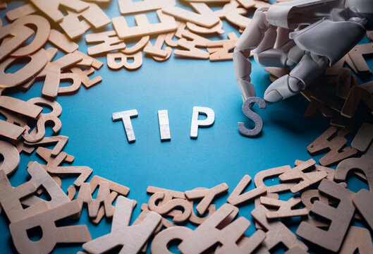 Robot hand arranging wooden letters to form Tips on blue background
