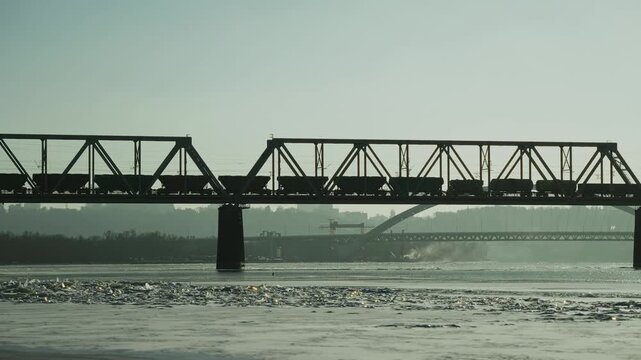 Cargo Freight Train Crossing Railway Bridge Over Frozen River. Rail Logistics And Delivery
