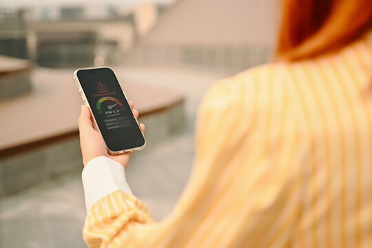 Woman shows PM2.5 air quality warning on smartphone while coughing in polluted city, highlighting health risks, smog danger, and need