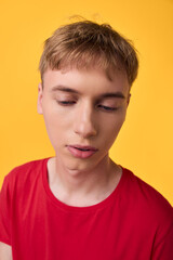 Naklejka premium Close up of a young male in a red shirt, contemplative expression against a bright yellow backdrop, conveying introspection and focus for fashion or lifestyle mood