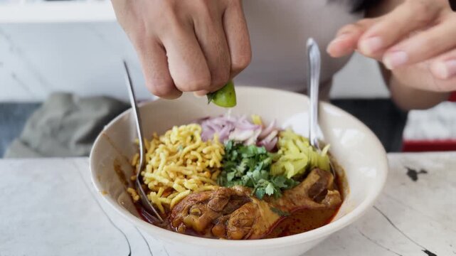 Asian street food chicken noodle soup close up. Woman squeezing lime to season Thai meal. Authentic Asian dish, fresh ingredients, traditional cuisine.