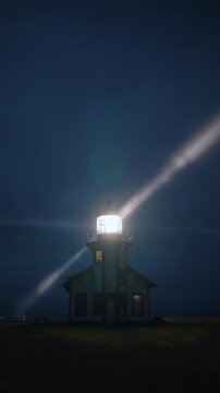Vertical Screen: Coastal lighthouse in vertical frame with rotating beam spreading across foggy night sky near Mendocino, California, USA creating moody cinematic atmosphere