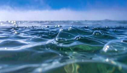 Zbliżenie na krystalicznie czystą powierzchnię oceanu z pęcherzykami powietrza pod błękitnym niebem i mglistym horyzontem w słoneczny dzień.
