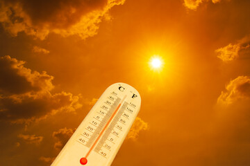 The thermometer against an orange sky. The thermometer is measuring the high summer temperatures, indicating scorching heat from global boiling.  © Chandet