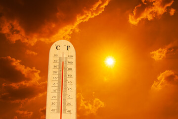 Fototapeta premium The thermometer against an orange sky. The thermometer is measuring the high summer temperatures, indicating scorching heat from global boiling. 