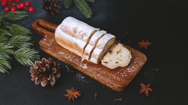 Sliced Classic Christmas Stollen dusted with powdered sugar on wooden board with pine cones