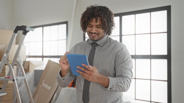 Man holding blue tablet tapping with right hand in building with moving boxes and ladder; new home optimism.