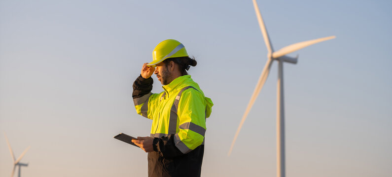 Engineer man working with tablet at windmill farm Generating electricity clean energy. Wind turbine farm generator by alternative green energy.