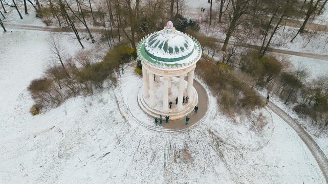 Smooth drone pan highlighting the Monopteros temple in Munich&rsquo;s English Garden, surrounded by snow and glowing in soft winter morning sunlight.