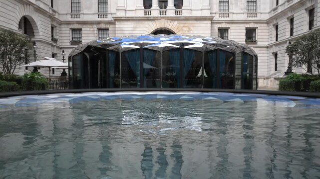 A serene view of the modern cafe exterior mirrored in a still water installation outside the historic Old War Office building on a bright spring day