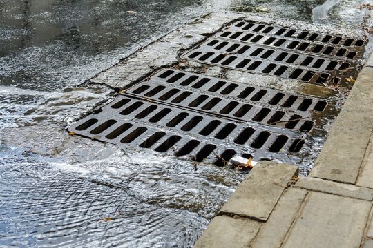 Stormwater rushing through metal grates along a curb, illustrating urban runoff and water management.