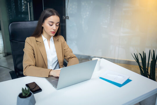 businesswoman sitting at desk in modern office using laptop while working