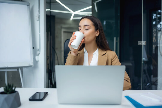Young woman sitting in office, drinking coffee for productiveness